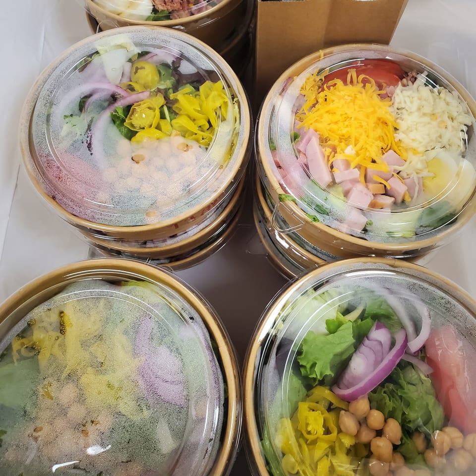 Four deli salads in clear plastic containers, filled with fresh vegetables, chickpeas, and meats.