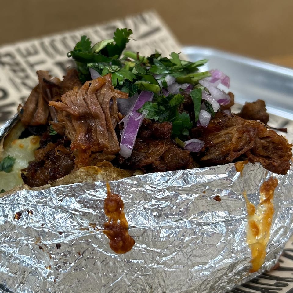 Close-up of a Field House Deli sandwich, wrapped in foil, filled with meat, cilantro, and red onions.