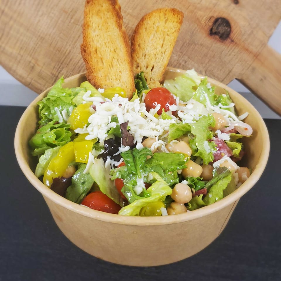 A Field House Deli salad with lettuce, tomatoes, chickpeas, peppers, olives, cheese, and croutons.